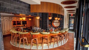 A bar area with wooden stools, a bar counter, and a large mirror. - The Merchant Hotel Lower East Side (New York)