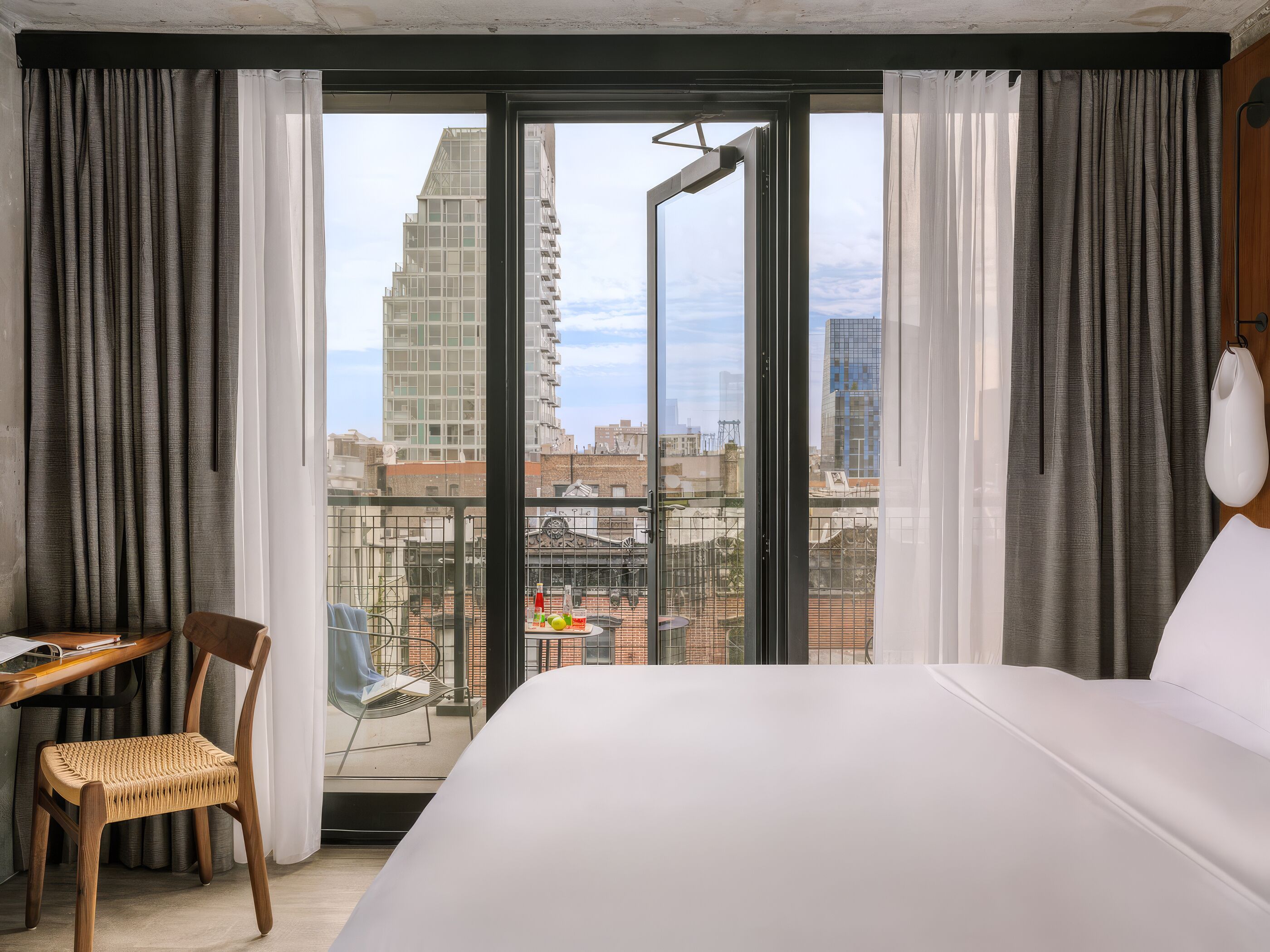 Ett hotellrum med en säng, ett skrivbord, en stol och en balkong med utsikt över staden.