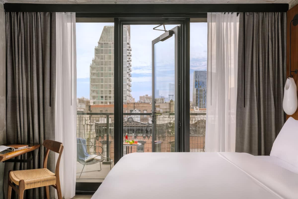 A hotel room with a bed, a desk, a chair, and a balcony with a city view.