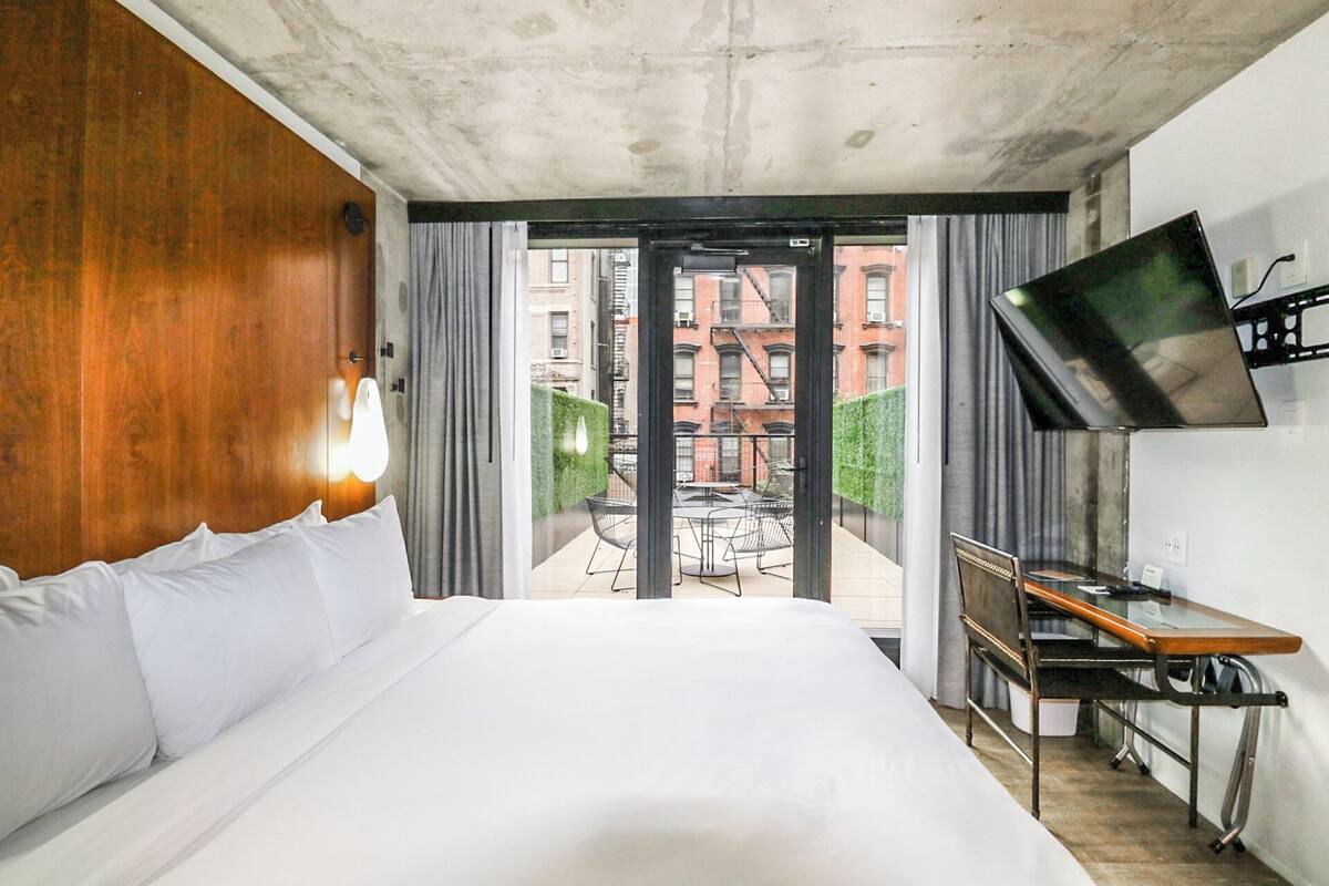 A hotel room with a large bed, a desk, a TV, and a view of the city through the window.