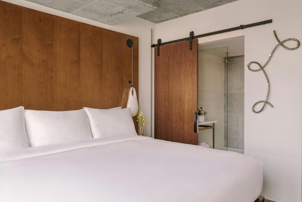 A bedroom with a large bed, wooden headboard, a sliding door, and a small bathroom visible through the door.