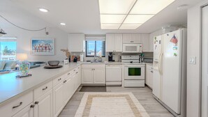 Una cocina moderna con armarios blancos, una isla central, microondas, horno y refrigerador.
