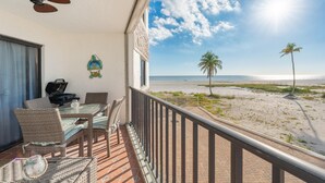Un balcón con mobiliario de mimbre, ventilador de techo y vista a la playa y al océano.