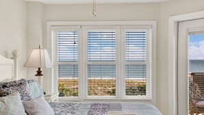 A bedroom with a large window, a bed with patterned bedding, a bedside lamp, and a view of the outdoors. - Superb 3-bedroom ocean view condo located within walking distance to everything! (Tybee Island)