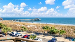 A beach view with a pier extending into the ocean, parking lot, and beachgoers. - Superb 3-bedroom ocean view condo located within walking distance to everything! (Tybee Island)