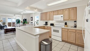A modern kitchen with white cabinets, a central island, and a stainless steel trash can. - Superb 3-bedroom ocean view condo located within walking distance to everything! (Tybee Island)