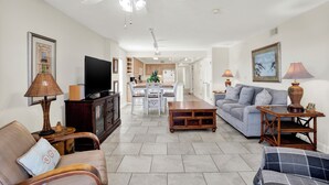 A spacious living room with a sofa, a television, and a dining area in the background. - Superb 3-bedroom ocean view condo located within walking distance to everything! (Tybee Island)