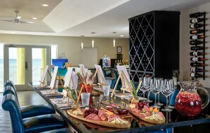 A bar area with a long counter, wine bottles on the wall, and a variety of cheeses and meats on platters. - Castaways Cove Beachfront Two Bedroom Condo Two Bathroom Condo (East End)