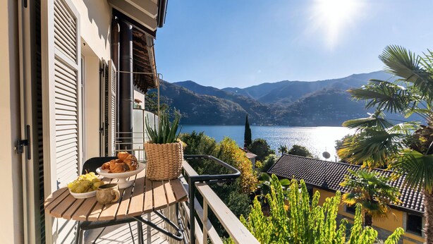 Un balcon avec une table préparée pour le petit-déjeuner, offrant une vue sur un lac et des montagnes.