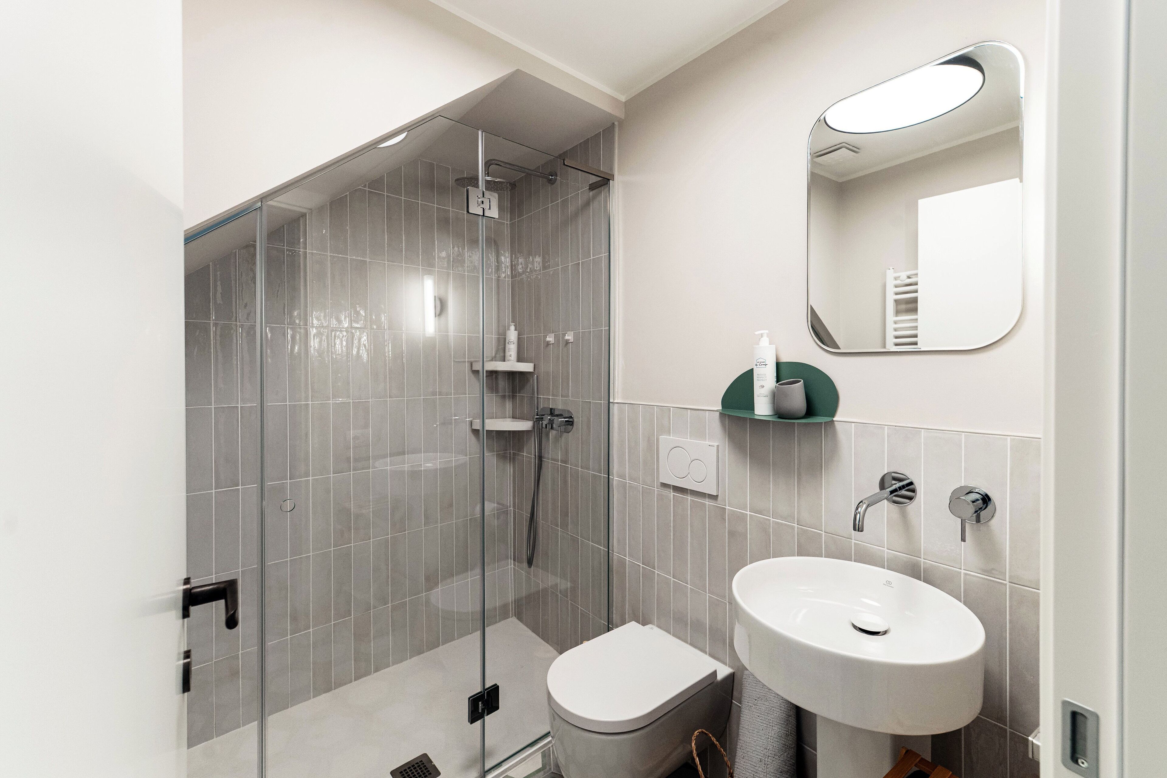Ein modernes Badezimmer mit einer gläsernen Duschkabine, einem weißen Waschbecken und einem Spiegel darüber.