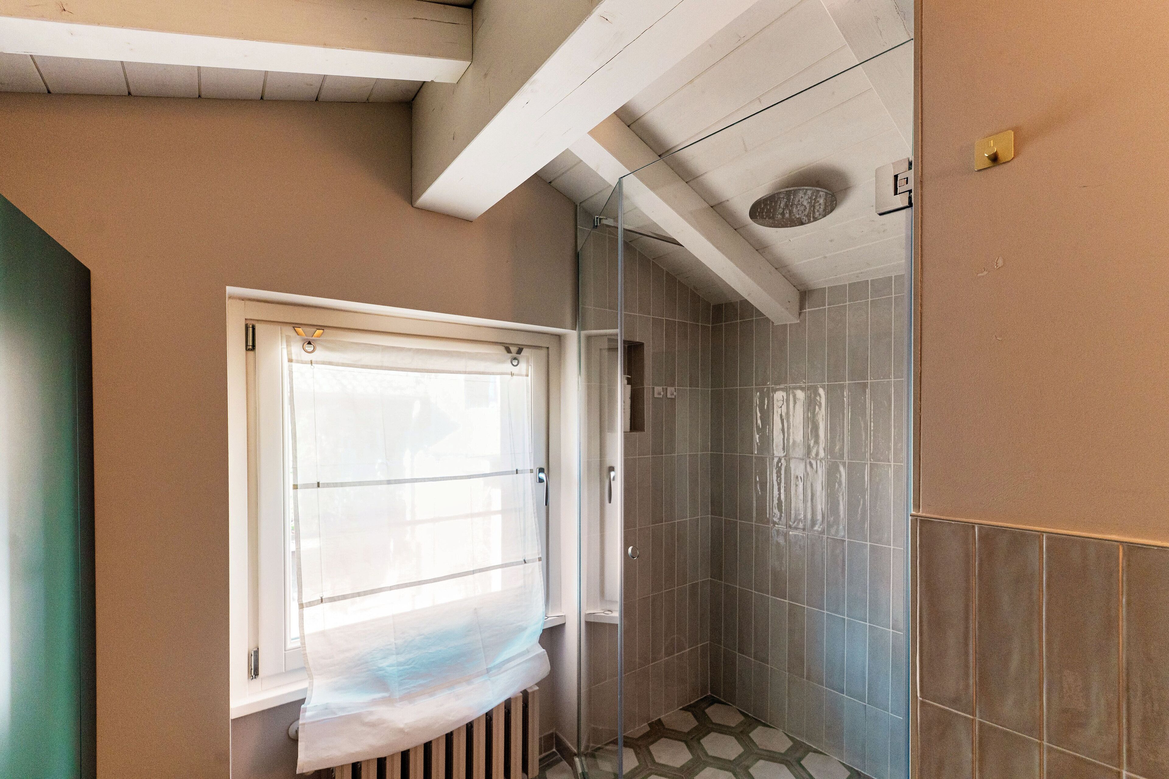 A bathroom with a shower, a window with a curtain, and tiled walls.