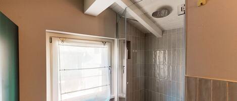 A bathroom with a shower, a window with a curtain, and tiled walls.