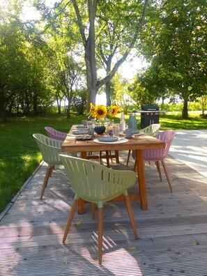An outdoor dining area with a wooden table and chairs, surrounded by greenery and trees.