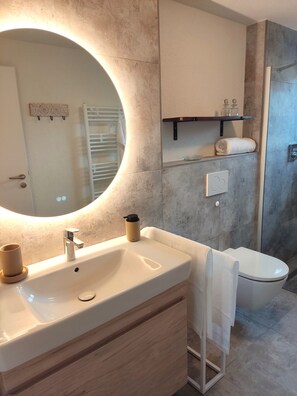 Un baño moderno con un espejo grande, un lavamanos, un inodoro y una ducha.
