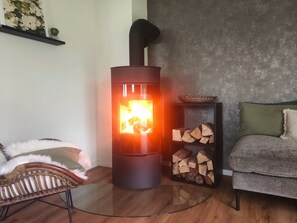 Ein modernes Wohnzimmer mit Kaminofen, Glastisch, Korbstuhl und grauem Sofa.