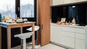 Una cucina moderna con un tavolo di legno, sedie bianche e vista sugli edifici attraverso una finestra.