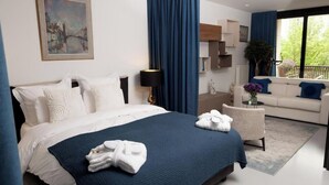 Una camera d'albergo moderna con un letto grande, un'area salotto con divano e poltrone, un balcone con vista e un quadro appeso al muro.