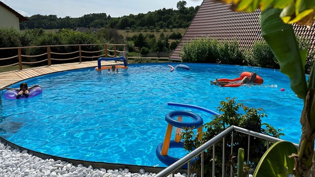 Ein Schwimmbecken mit Holzterrasse, Rutsche und aufblasbaren Spielzeugen.