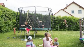 Ein Trampolin in einer grünen Freifläche, im Hintergrund ein Haus.