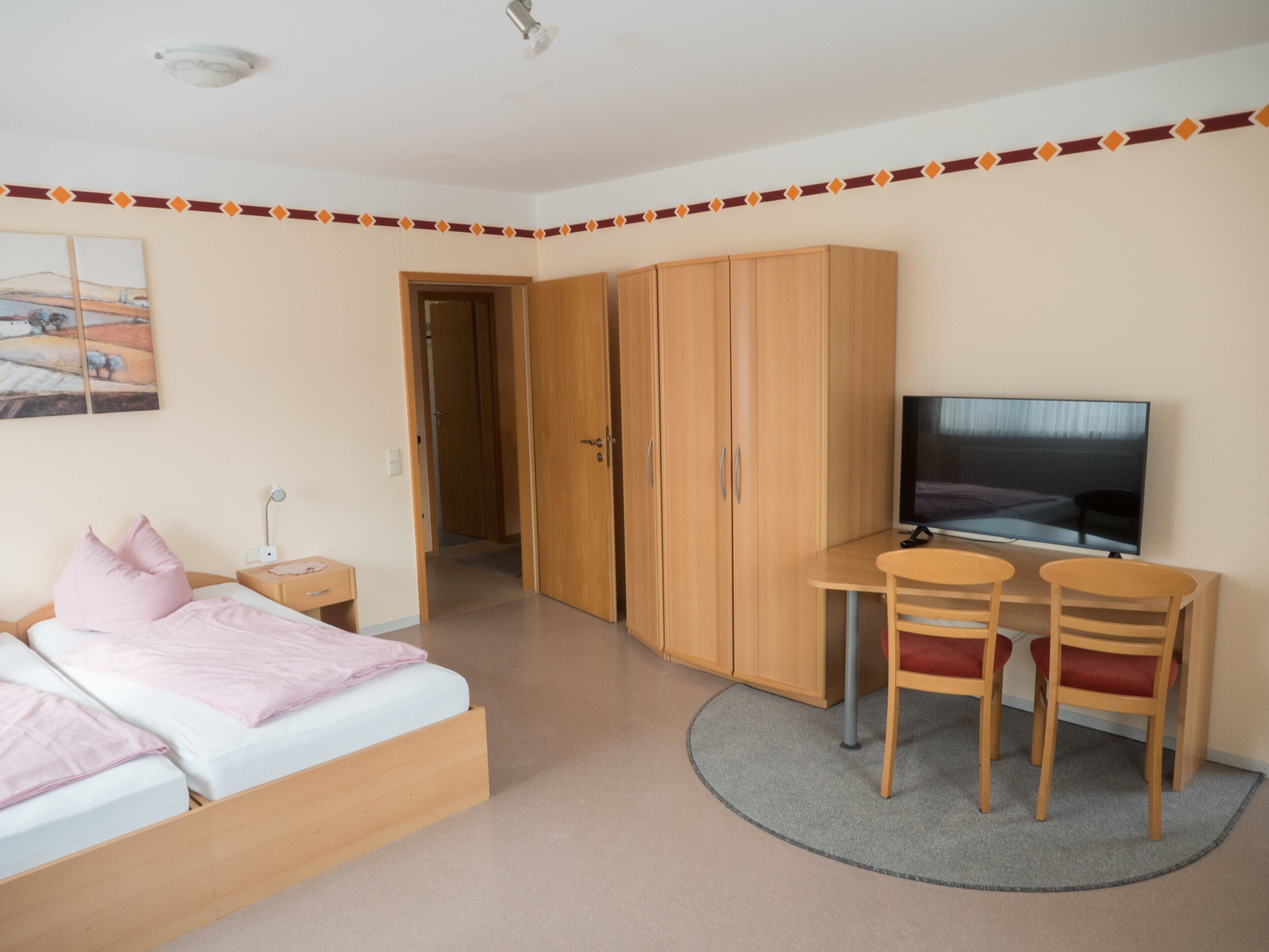 Une chambre à coucher comprenant un lit, un bureau avec deux chaises, une télévision et une armoire.