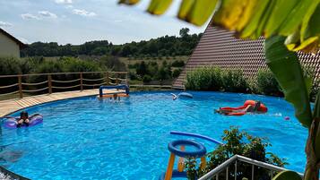 Une piscine avec une terrasse en bois, un toboggan et des jeux gonflables.