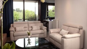 A modern living room with two beige sofas, a glass coffee table, and a view of a balcony with greenery. - Suite aux Anges N°3 (Duplex) (Antwerpen)