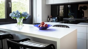 A modern kitchen with a white countertop, a blue bowl of fruit, and a vase of blue flowers. - Suite aux Anges N°3 (Duplex) (Antwerpen)