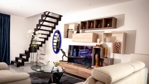 A modern living room with a staircase, a flat-screen TV, and built-in shelving. - Suite aux Anges N°3 (Duplex) (Antwerpen)