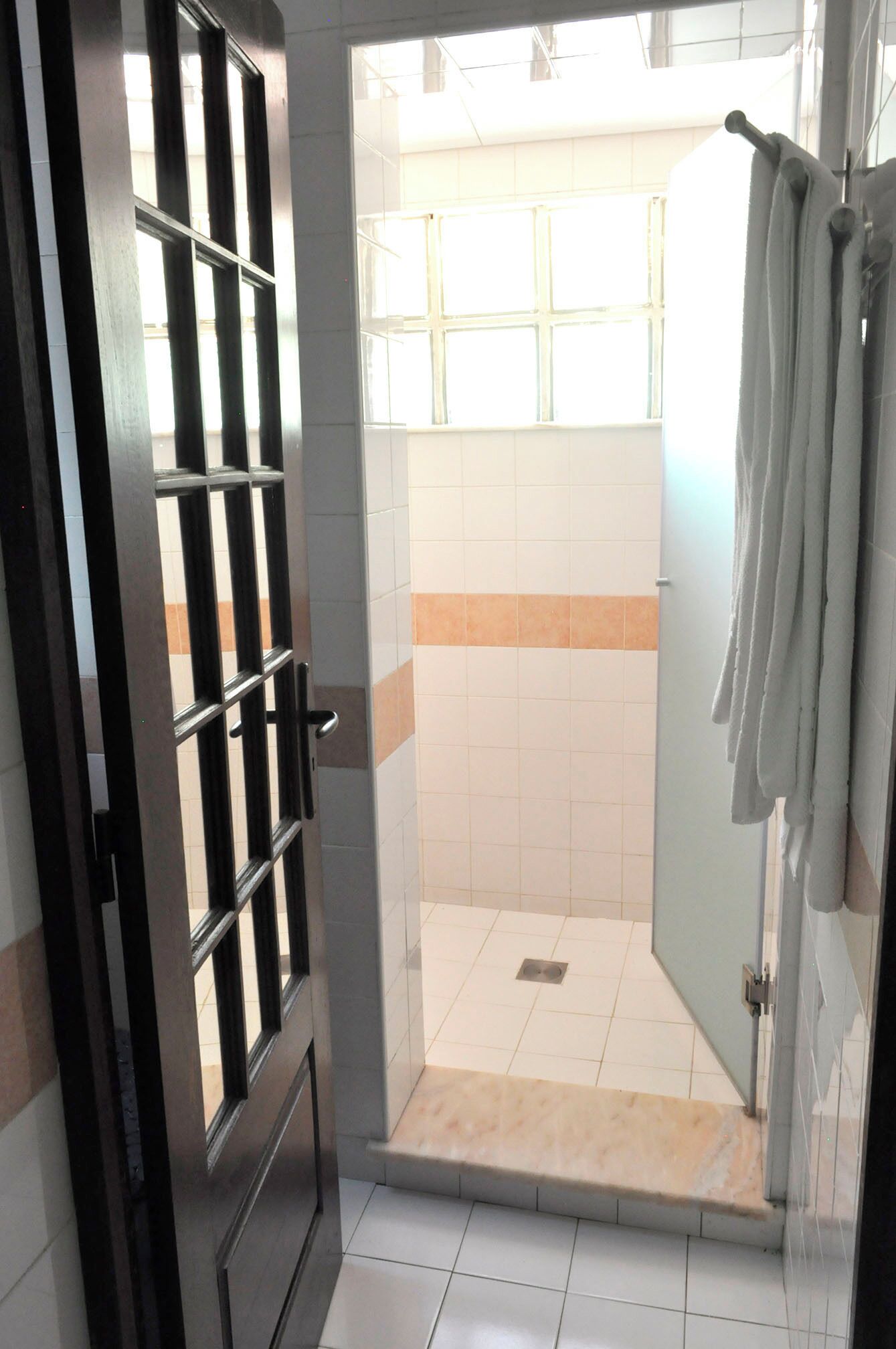 A shower area with a tiled floor, a metal door with a security bar, and a towel hanging on the wall.
