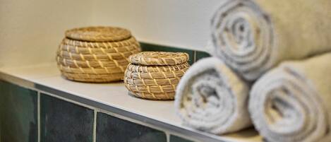 A bathroom with a tiled wall, a woven basket, and rolled towels.