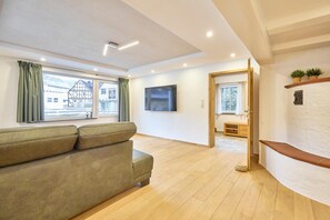 Un salón con sofá, televisor de pantalla plana, suelo de madera y vistas a edificios.