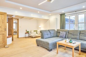 En rummelig stue med en grå modulsofa, et træbord og et vindue med gardiner.