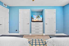 A bedroom with a TV on a dresser, a bed with a white quilt, and a blue wall. - Gulf and Bay Club-B110- Just 5 minutes from Siesta Beaches! (Siesta Key)