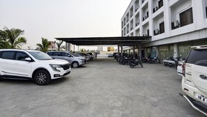 En parkeringsplats med flera bilar och motorcyklar, en överbyggd gångväg och en flervåningsbyggnad med balkonger.
