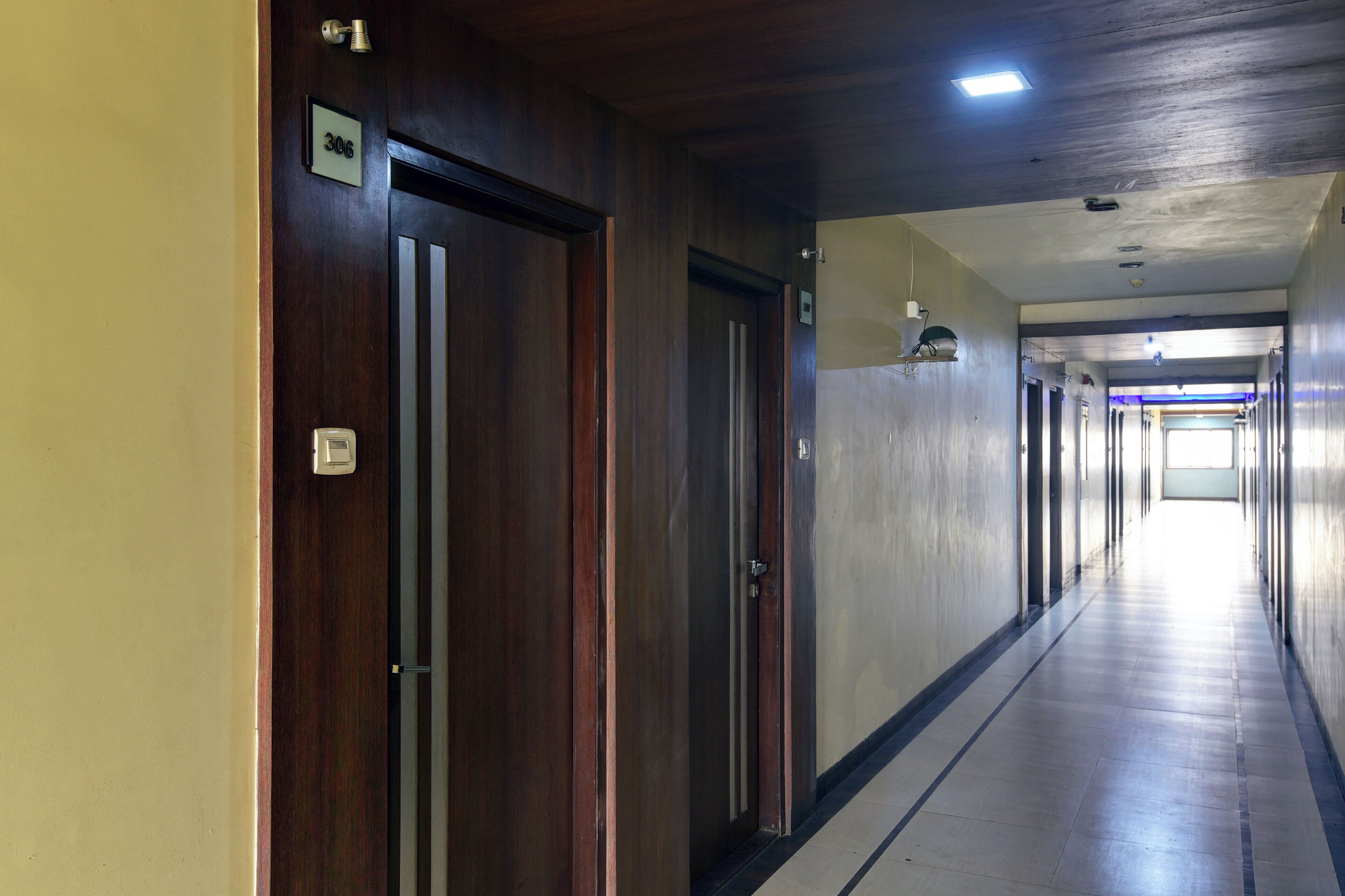 A long, narrow hallway with wooden doors on the left and a bright exit at the end.