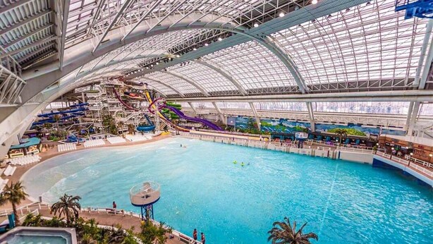 Ein Indoor-Wasserpark mit großem Pool, Wasserrutschen und einem überdachten Bereich mit Sitzgelegenheiten.