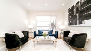 Ein modernes Wohnzimmer mit großem Fenster, zwei schwarzen Samsofas, einem weißen Couchtisch und einem großen abstrakten Gemälde an der Wand.