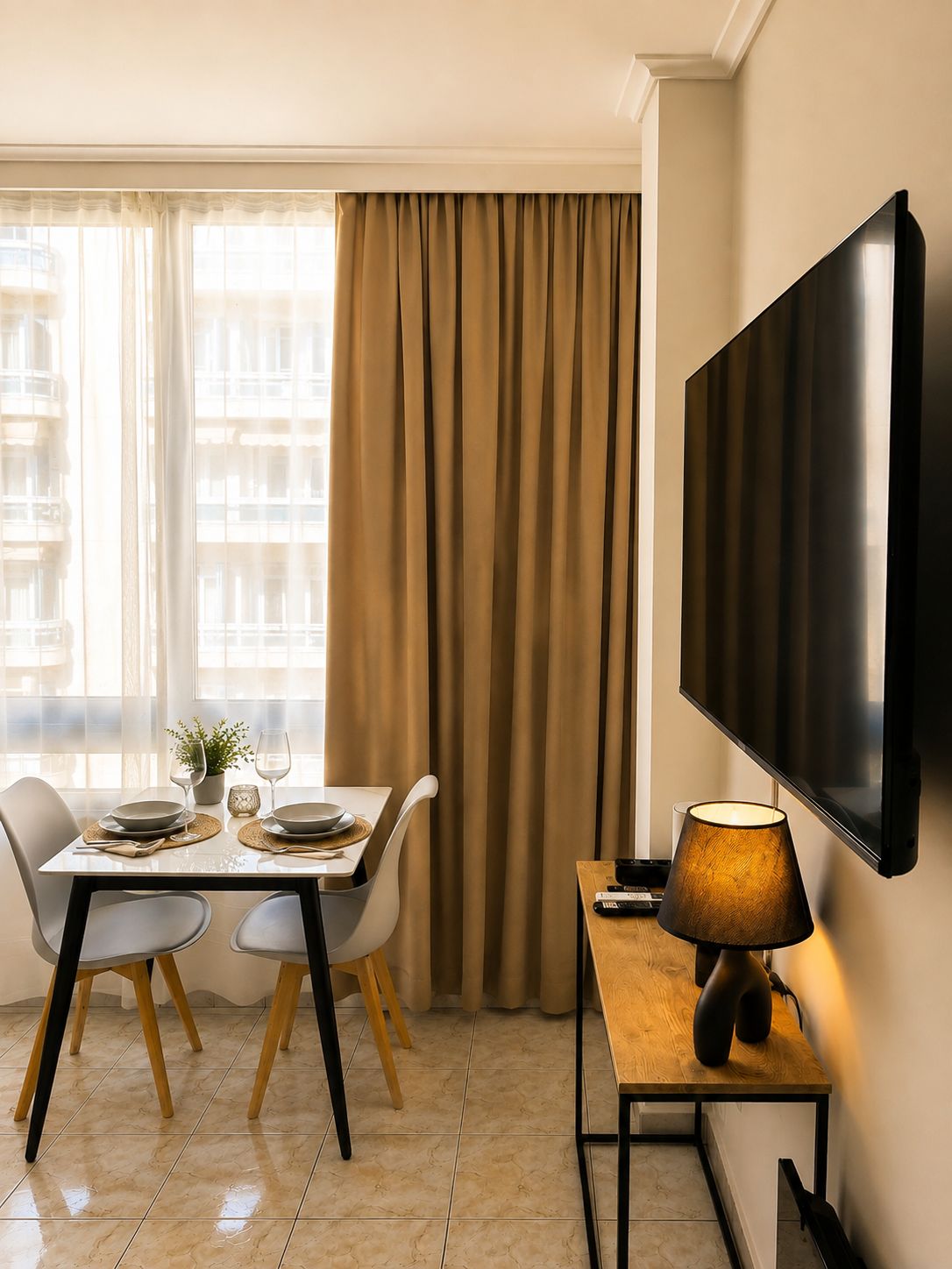 Ein stilvoller Essbereich mit Tisch für zwei Personen, einem Fernseher auf einem Schrank und einem Fenster mit Vorhängen.
