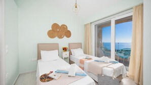 Ein Hotelzimmer mit zwei Betten, Meerblick, einem Balkon mit Stühlen und einer Hängelampe.