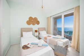 Een hotelkamer met twee bedden, uitzicht op de zee, een balkon met stoelen en een hanglamp.