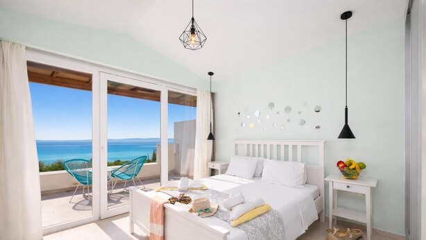 Ein Schlafzimmer mit Bett, Nachttisch mit Früchten, einem Sessel und Blick aufs Meer.