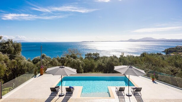 Une piscine bordée de chaises longues et dotée de parasols, offrant une vue sur la côte.