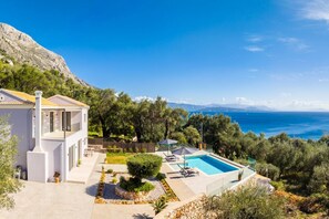 A modern villa with a swimming pool, surrounded by lush greenery and a view of the sea.
