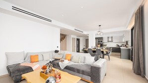 Un salon moderne avec un canapé d’angle, une table basse en bois et un coin repas avec une cuisine en arrière-plan.