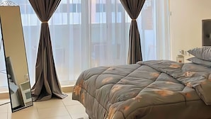 Ein Schlafzimmer mit einem Bett, einem Deckenventilator und einem großen Fenster mit Vorhängen.