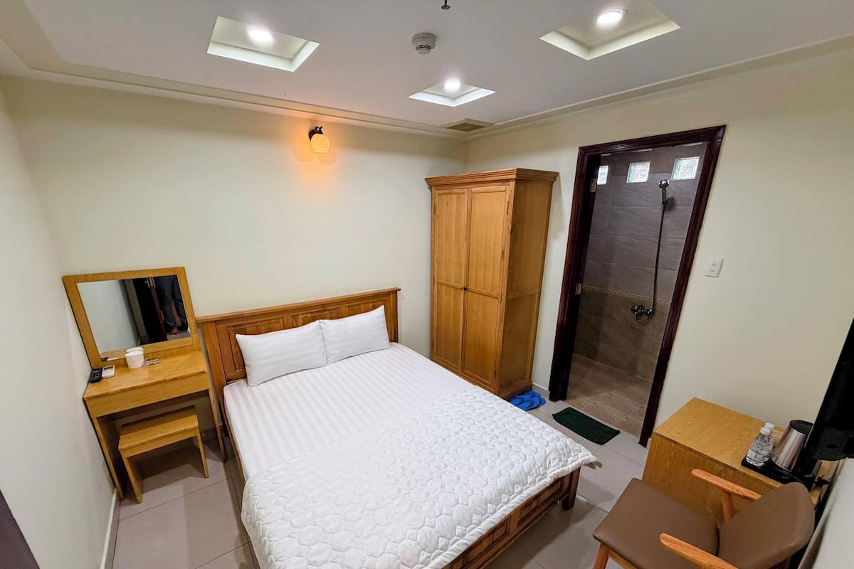 Un dormitorio con cama, un armario de madera, un escritorio con silla y un televisor.