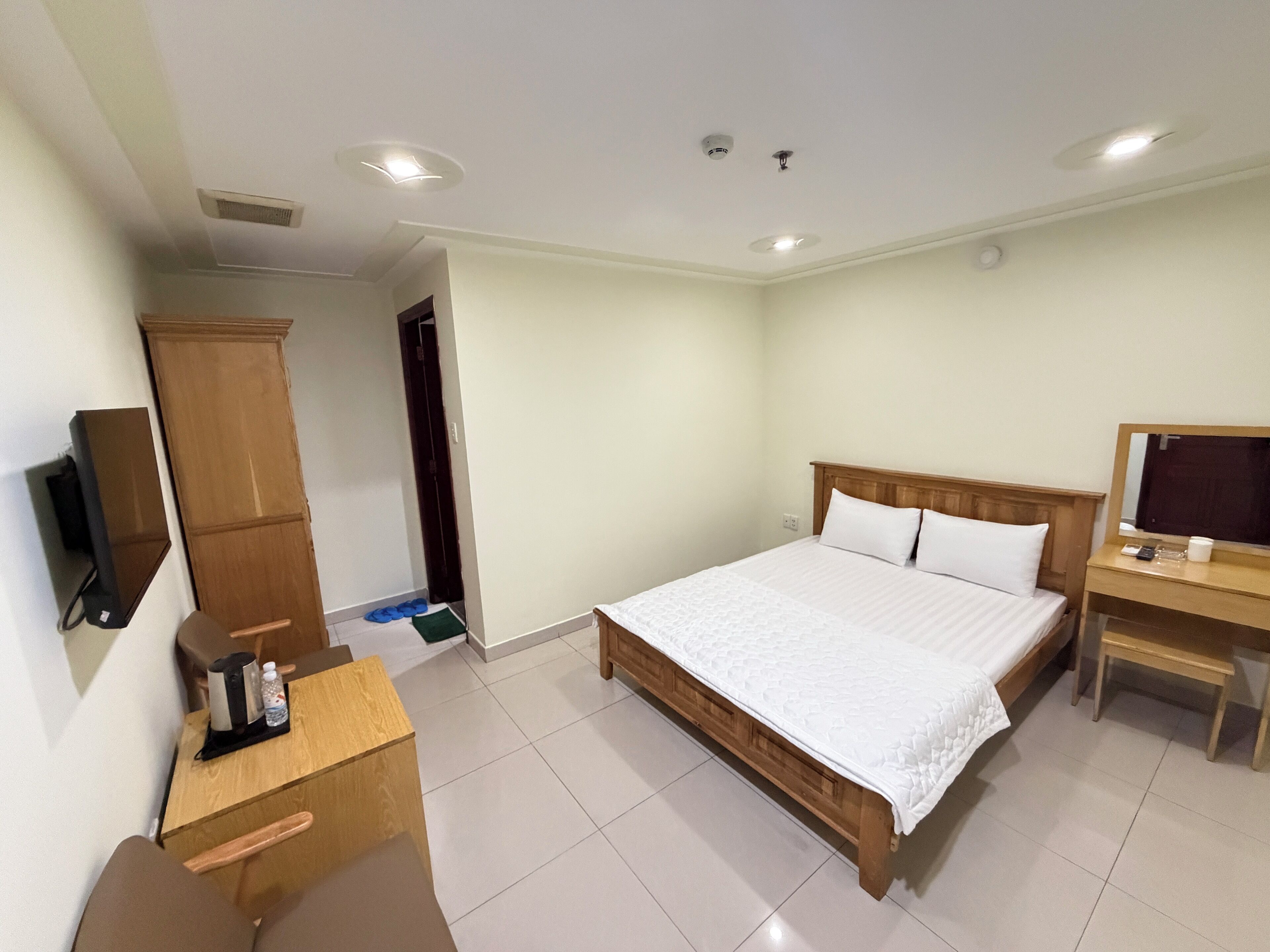 A hotel room with a bed, a wooden desk, a television, and a wardrobe.