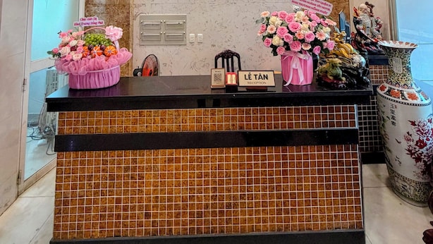 A hotel reception desk with a marble wall, a clock, and a sign that reads "Hoàng Tại Hotel".