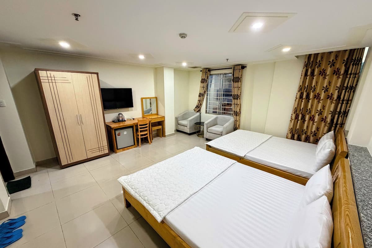 Habitación de hotel con dos camas, un escritorio con silla, un armario, televisor y ventana con cortinas.