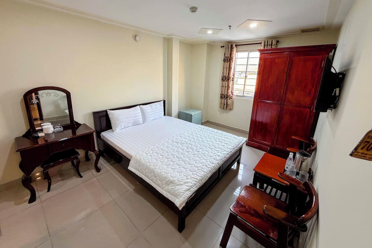 Una habitación de hotel con cama, cómoda de madera, espejo, armario y ventana con cortinas.